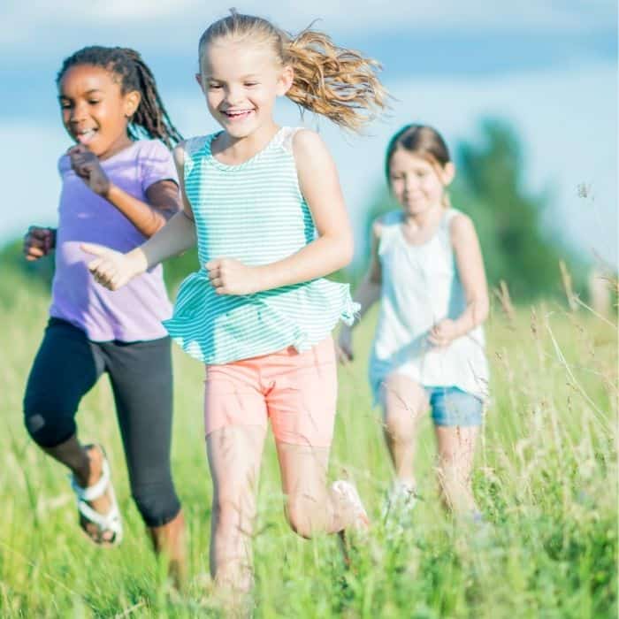 A group of homeschool children are participating in a community co-op. These three girls are running in a field together.