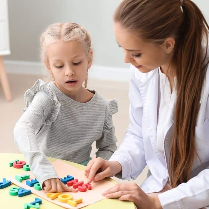 A mother is teaching her daughter how to read and spell using alphabet blocks.