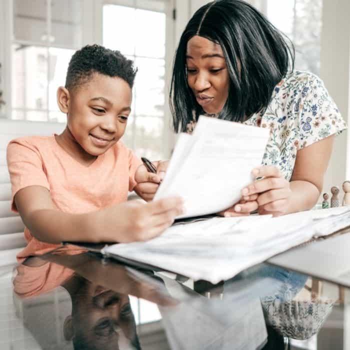 A mother teaching her son, while he reads his paperwork.