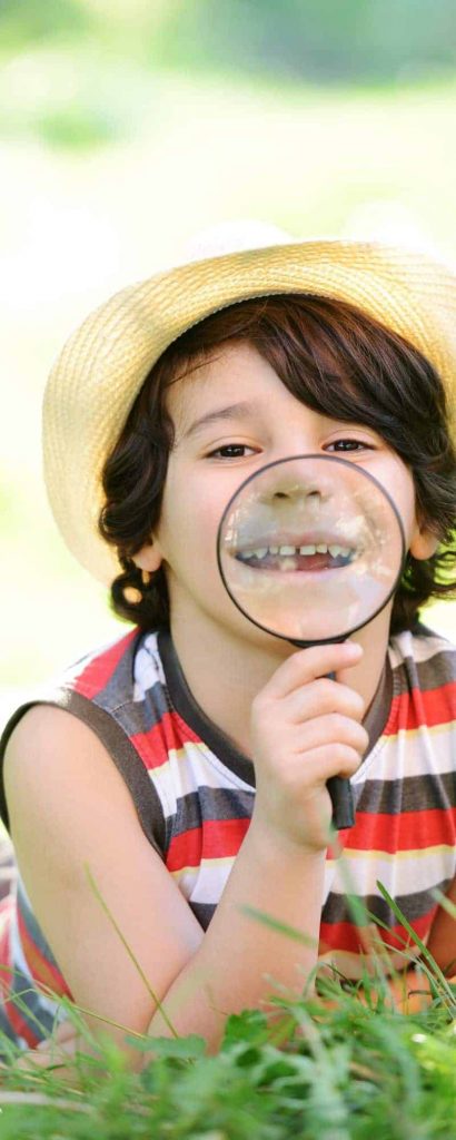A child playing with a magnifying glass in a field of grass.