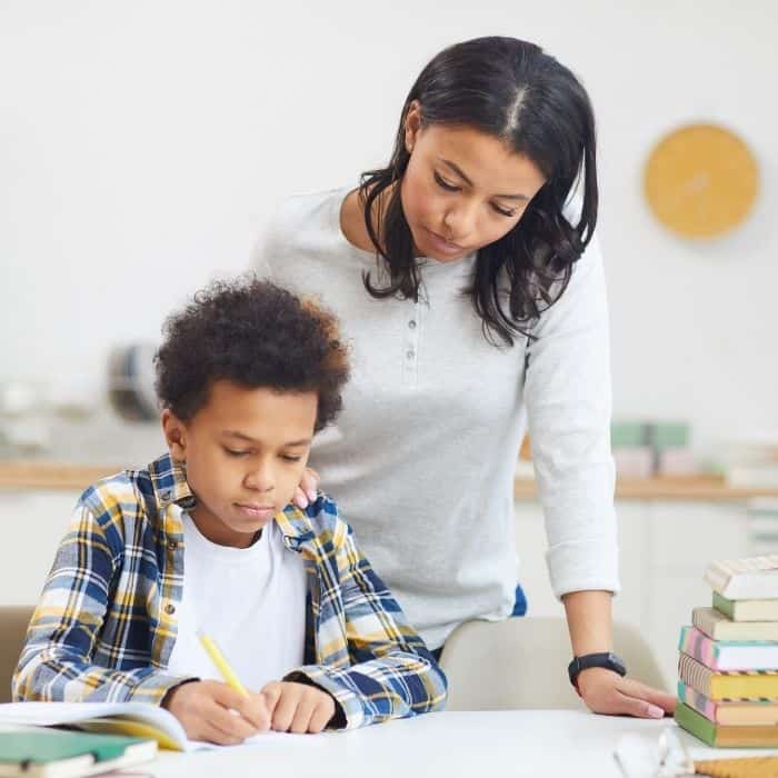 A mother is standing over the shoulders of her son as he completes his learning.