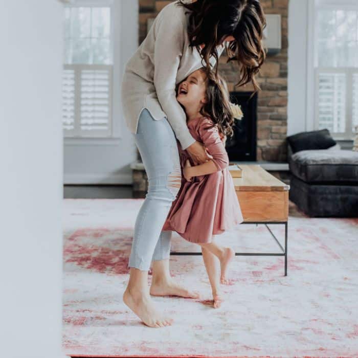 A mother dancing with her daughter at home in the living room.
