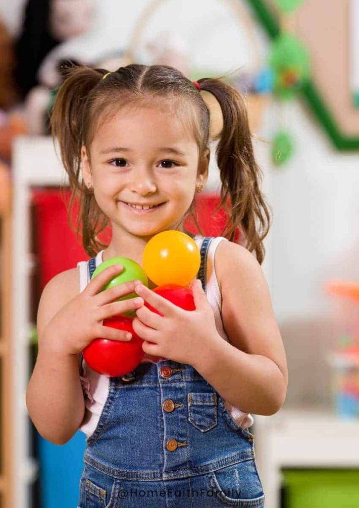 Preschooler holding different color balls and toys in class.