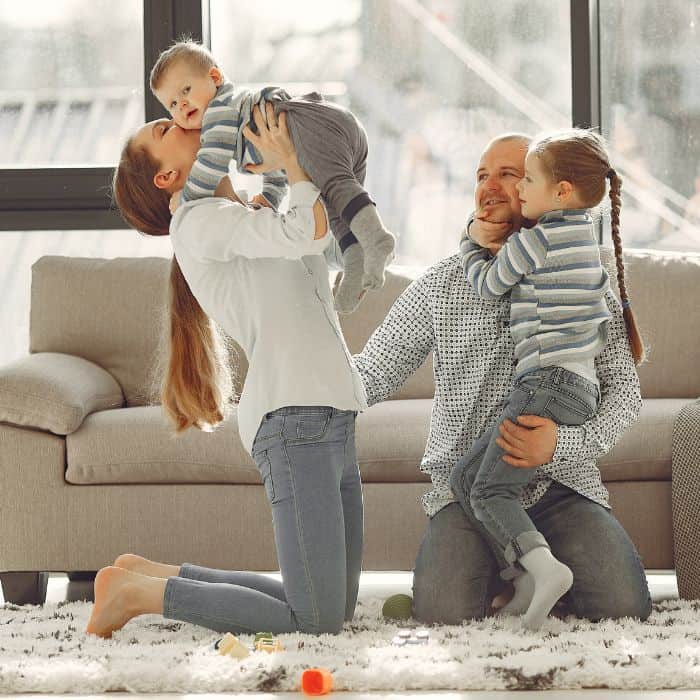 A family playing on the ground together. The father and mother are holding and hugging their children.