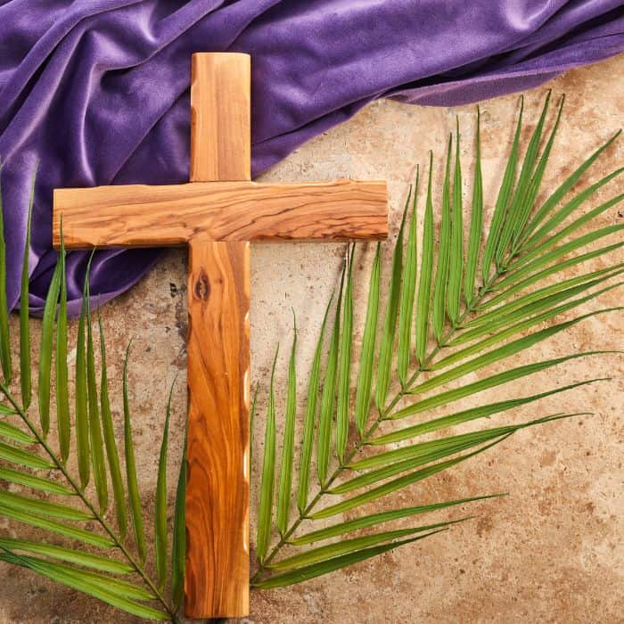 A wooden cross laid on top of palm leaves and a purple cloth.