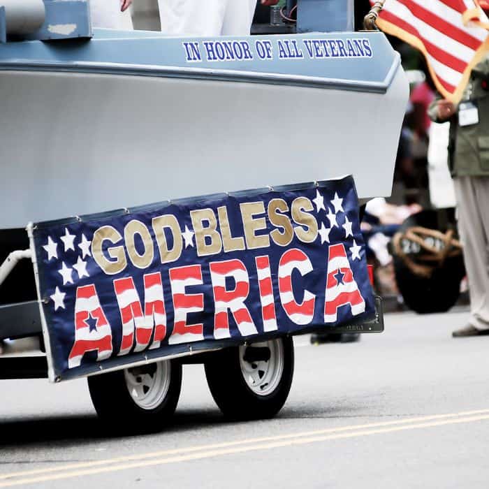 Back bumper of a car with a sign that reads "God bless America" in the parade.