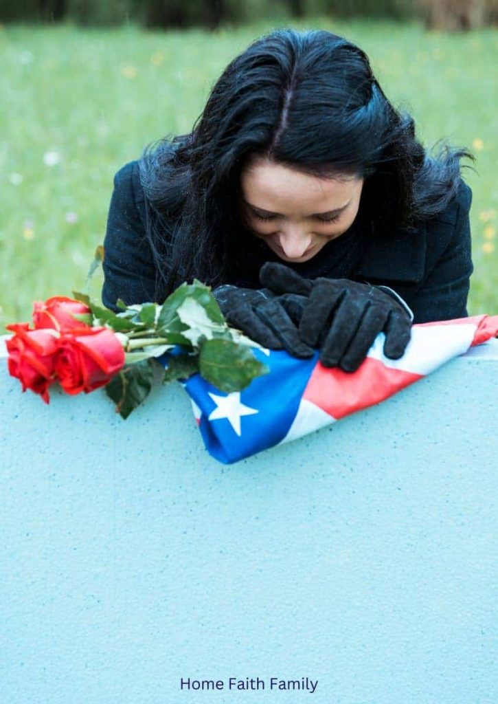 A woman mourning over the graveside of her fallen loved one who died in military service. The headstone is draped with an American flag and roses.