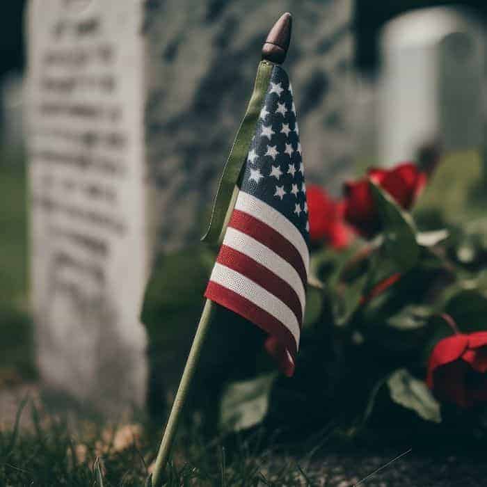 American flag and a bouquet of roses laid against the headstone of a fallen soldier.