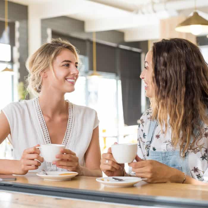 Two women drinking a cup of tea or coffee together. Both are smiling and happy.