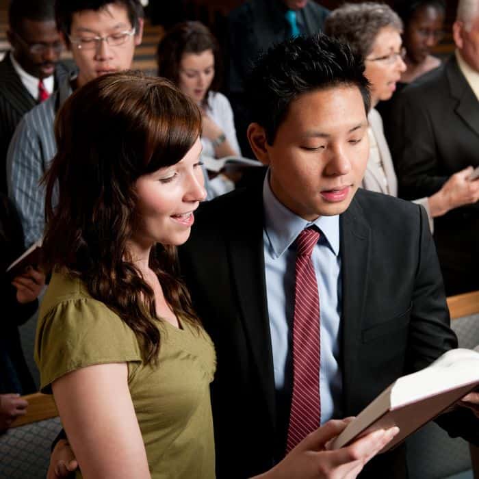 A husband and wife sitting next to each other in church singing a hymn.