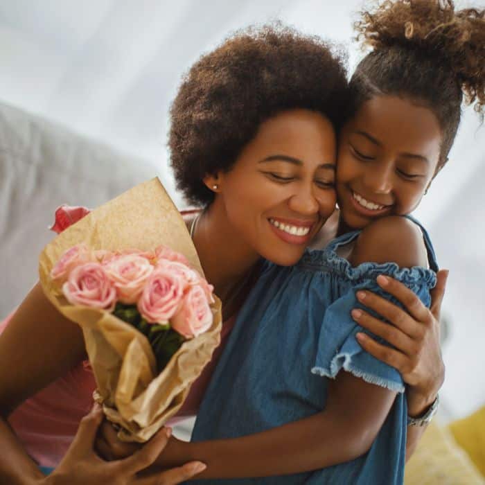 A daughter giving her mother a bundle of pink flowers. Both are hugging and smiling.