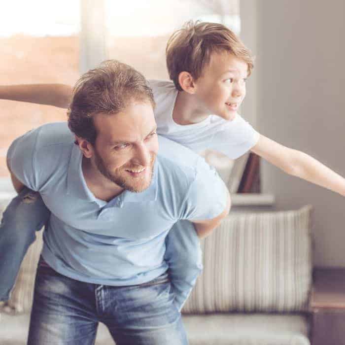 A dad giving his son a piggy back ride in their living room.