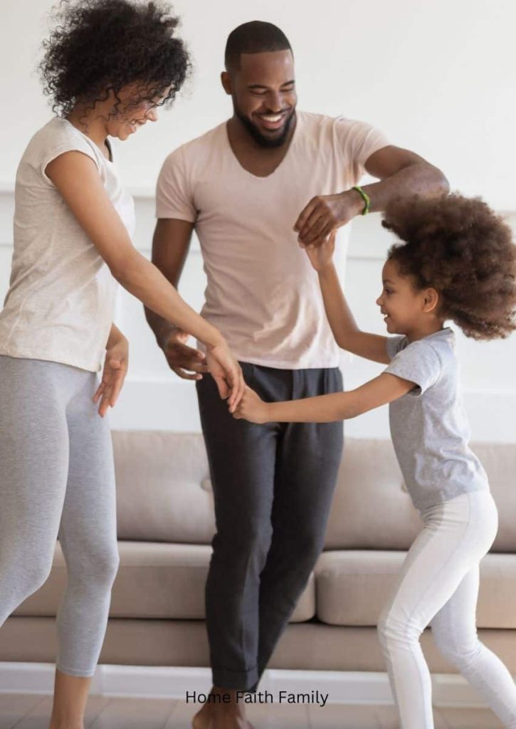 A husband and wife standing in the living room dancing with their daughter.