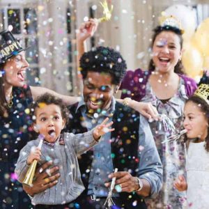 A family celebrating New Years Day and throwing confetti up into the air. The family is surrounded by loved ones.