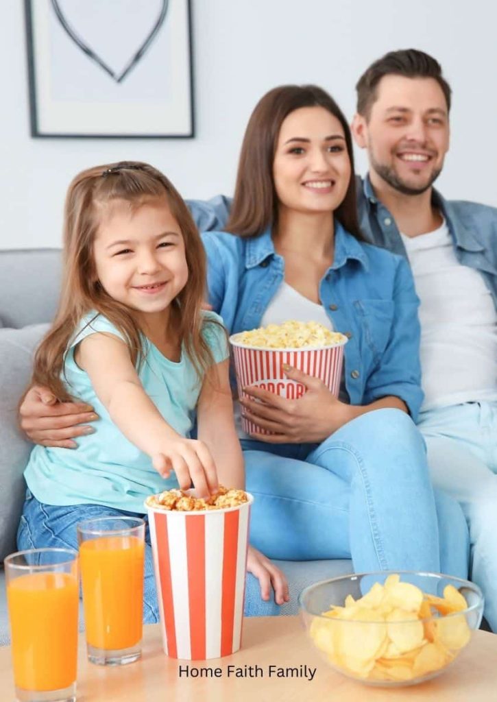 Family watching a movie together with popcorn, chips, and drinks.
