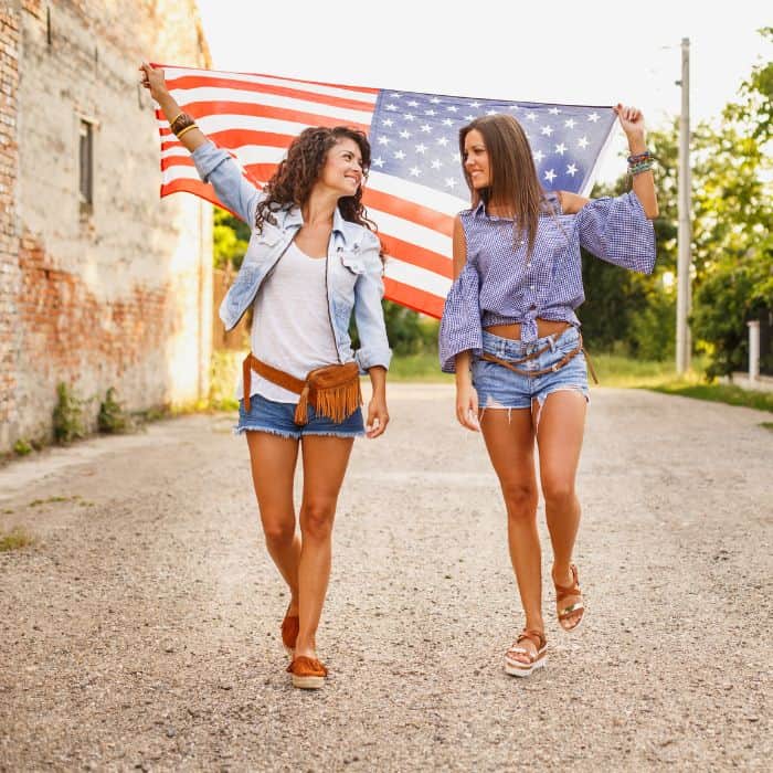 Two young ladies walking down the road with an American flag.