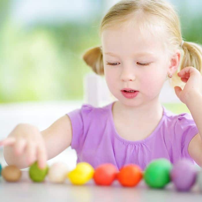 A little girl is playing with a row of colorful play doughs. 