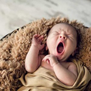 A newborn baby wrapped in a blanket. The baby is yawning.