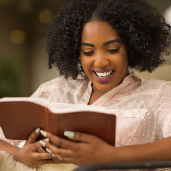 A joyful woman engrossed in reading a book with a smile on her face.