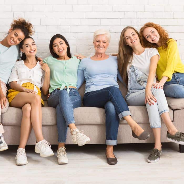 A group of happy, diverse women sitting closely together on a sofa, smiling and enjoying each other's company.