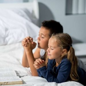 Siblings praying together with their Bible open.