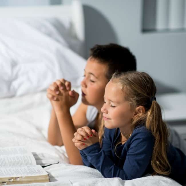 children praying together over an open Bible.