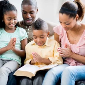 A mother and father in prayer and scripture reading with their daughter and son.