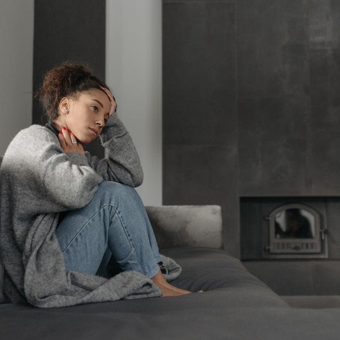 A woman is sitting on the couch. She looks sad.