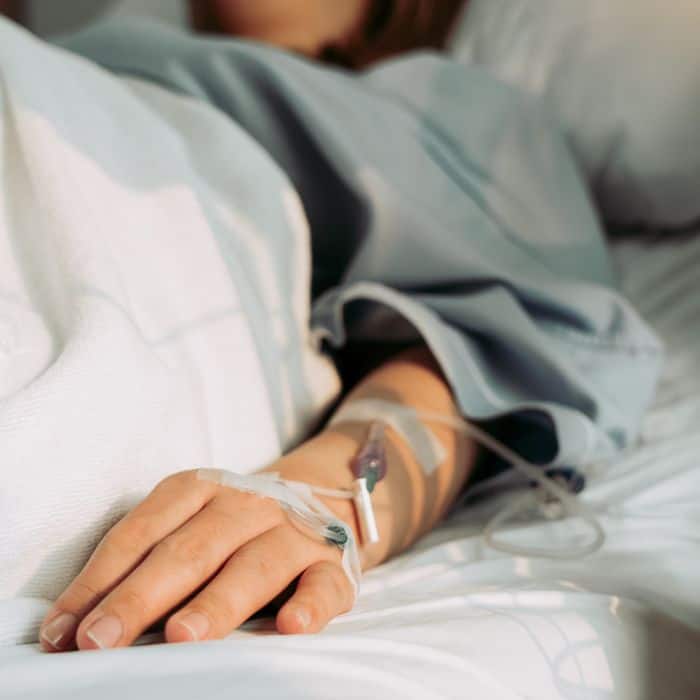 A woman has cords, needles, and other devices while laying in a hospital bed.