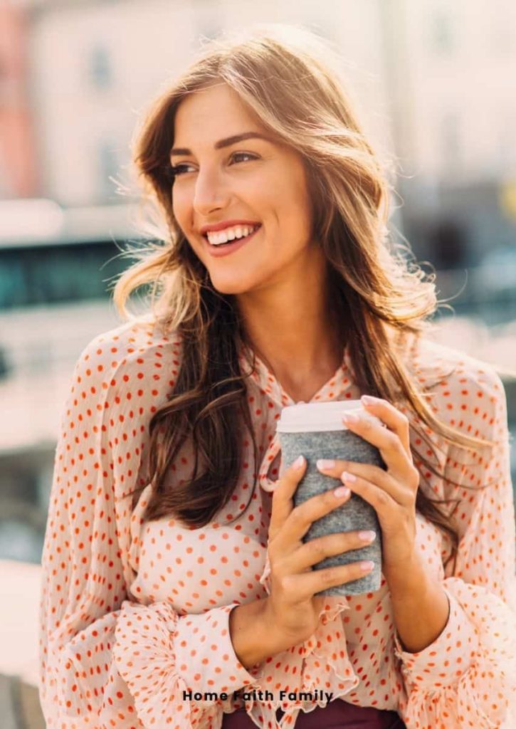 A woman holding a hot drink. She is dressed nicely and smiling.