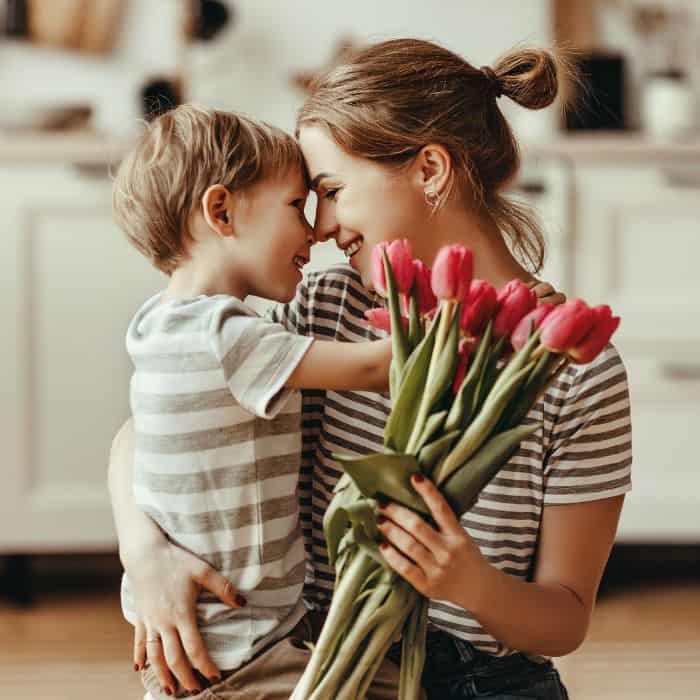 A mother is wrapping her arms around her young son. She's holding a bundle of tulips.