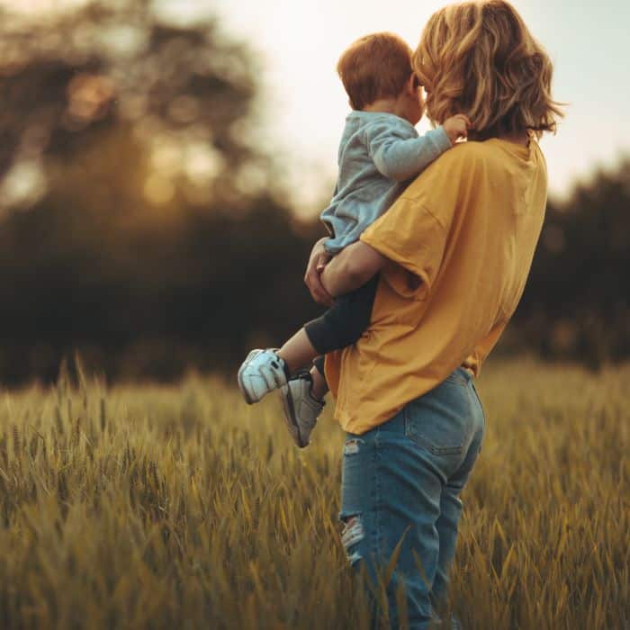 A mother holding her son in a grass field.