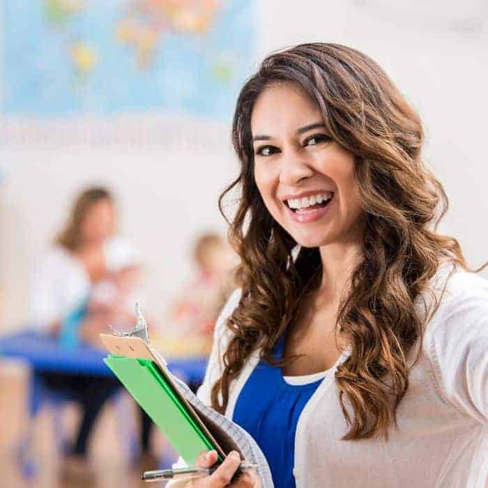 a preschool worker holding a notebook and smiling.