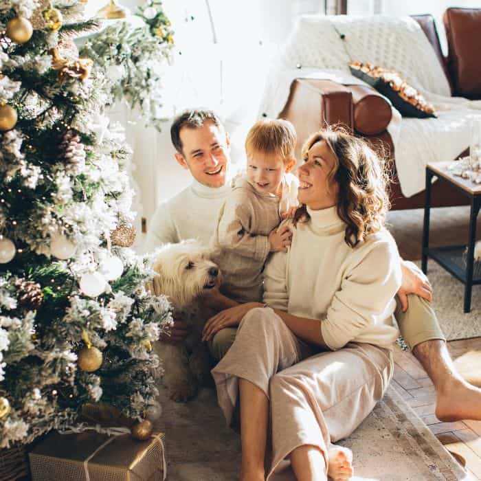 A husband, wife, and child sitting at the foot of a Christmas tree.