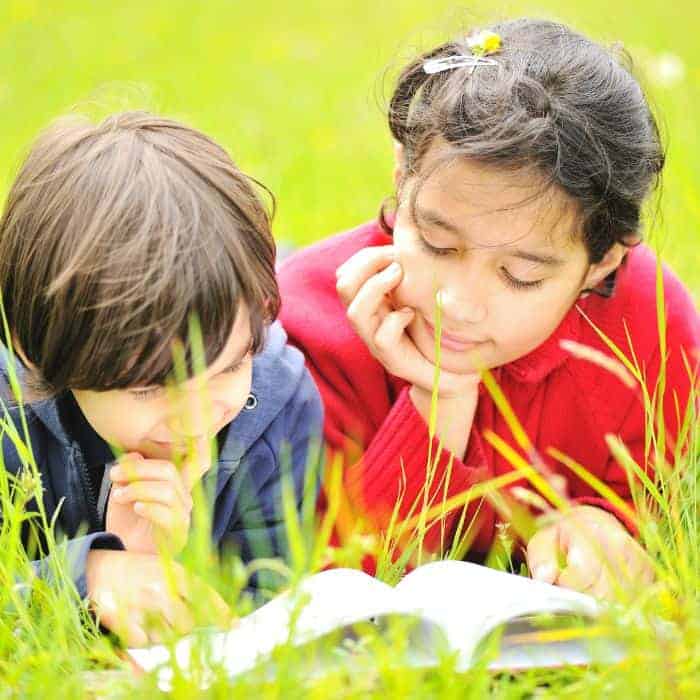 A brother and sister reading a book in a field of grass.