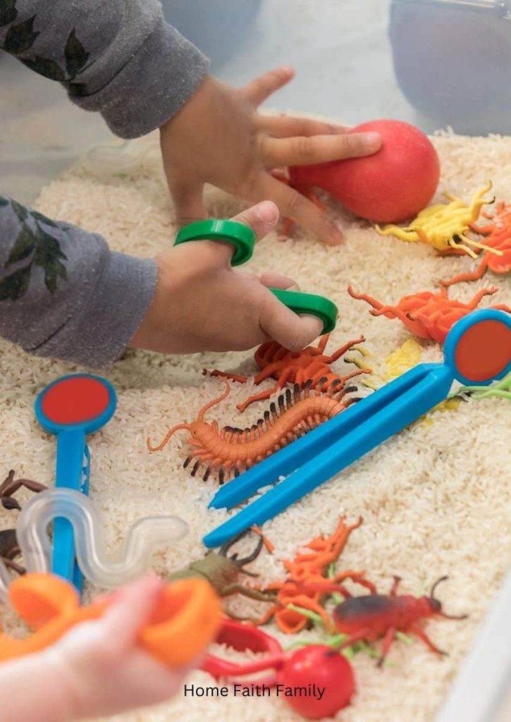 Small children playing in a sensory bin of sand and plastic toys.