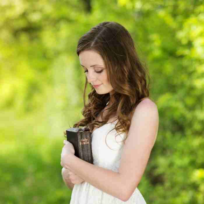 A woman in a white dress who is holding her Bible.