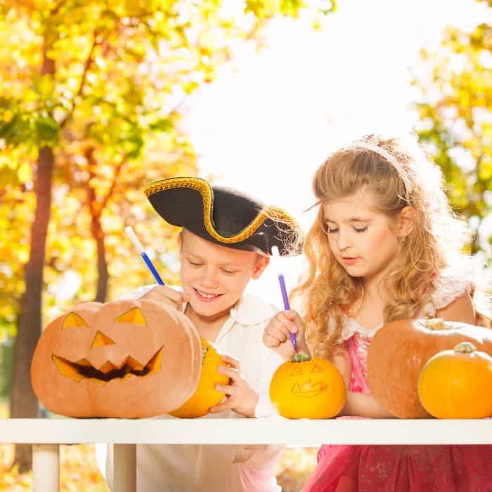 A little boy and a little girl carving Halloween pumpkins on a table. The children are dressed as a pirate and a princess.