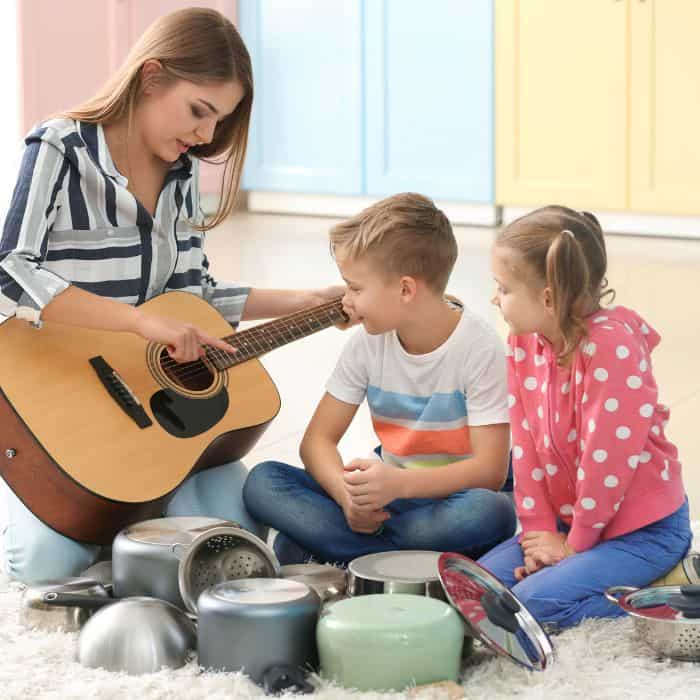 A mom playing the guitar with her children watching.