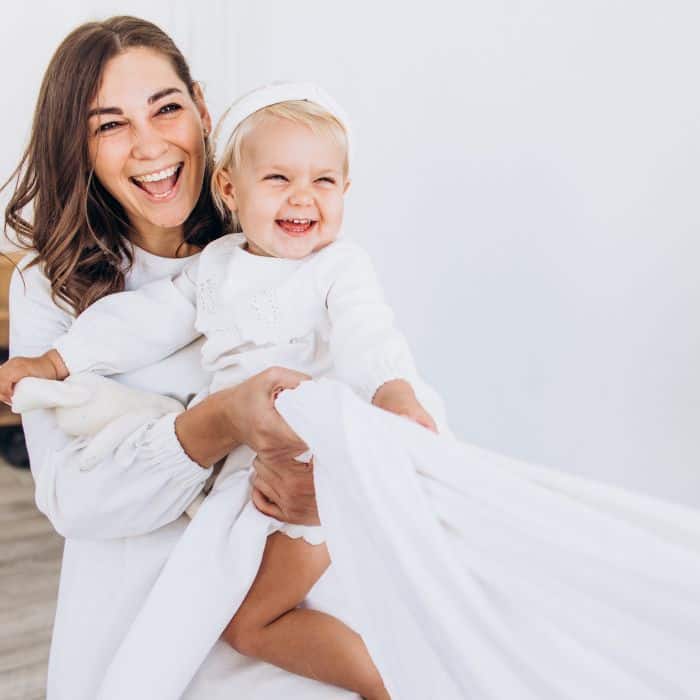 A mom and baby dressed in white smiling and playing.