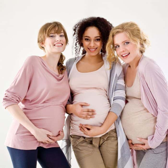 Three pregnant women standing next to each other showing the size of their bellies.