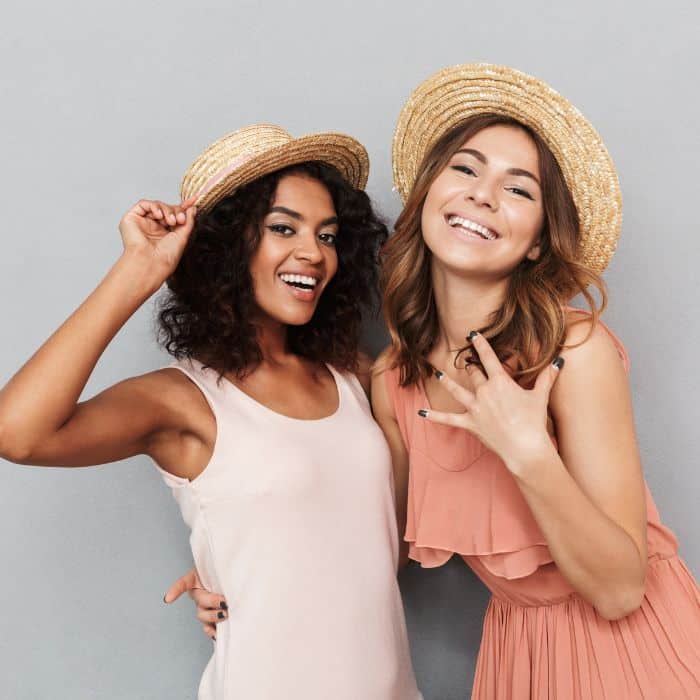 Two women in summer hats are smiling and laughing with each other.