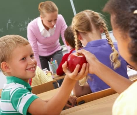 A little boy sharing an apple with a classmate.