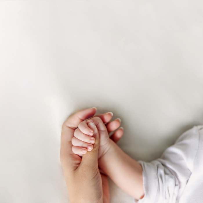 a small child's hand is clasping his mother's thumb in a tight squeeze.