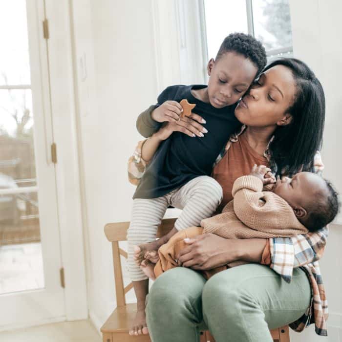 A mother surrounded by her children. She is embracing an older son and cuddling with an infant on her lap.