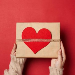 A woman holding a present box with a red heart on the top of the box.