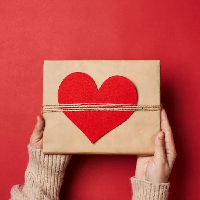 A woman holding a present box with a red heart on the top of the box.