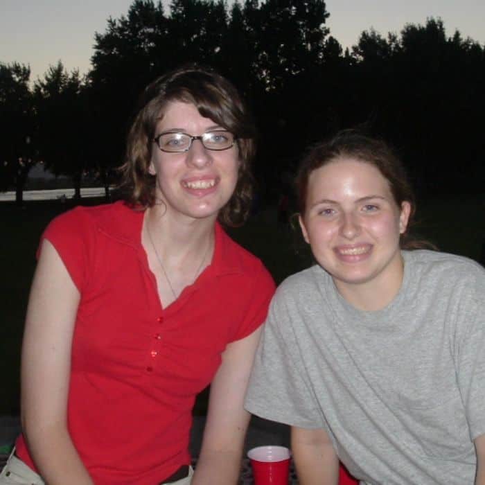 Two girls sitting at the park together. Both are smiling.