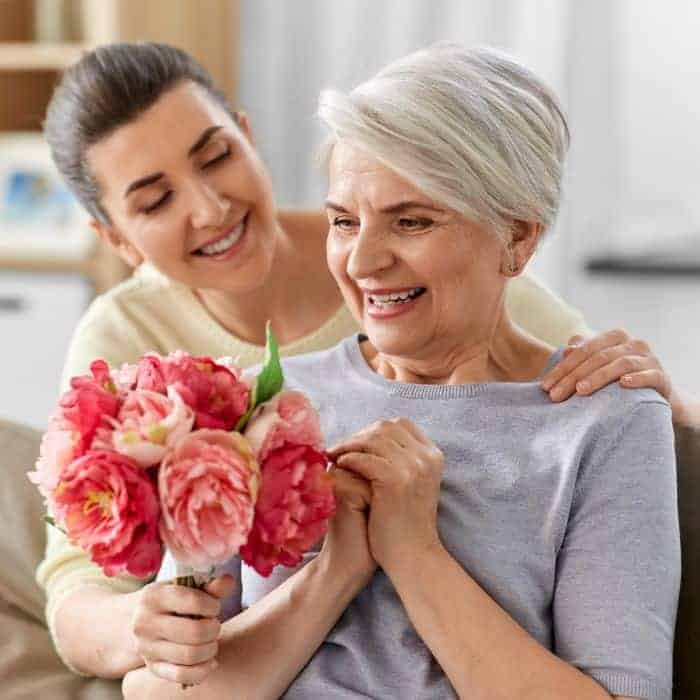 A daughter is handing her aging mother a bundle of pink flowers.