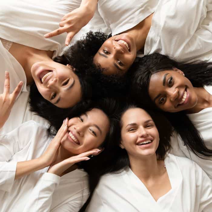 A group of women all wearing white. They're laying on the ground looking up and smiling.